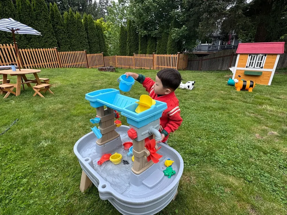 Preschoolers at Kido Heaven Child Care in Bothell, WA, pour water using containers in an outdoor STEM water play activity, fostering science inquiry and sensory development.
