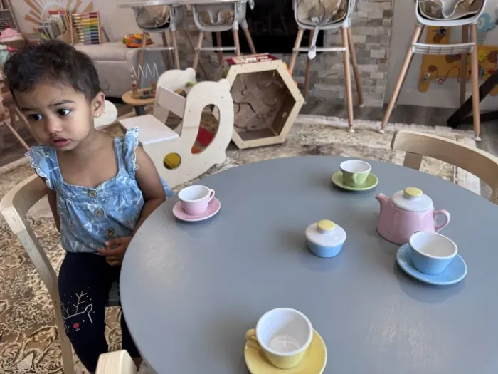 A toddler at a pretend tea party table with little cups and saucers