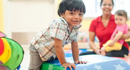 A smiling little boy playing on a mat with his teacher